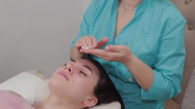 Kadın masaj terapisti masaj salonunun müşterisine yüz masajı yapar..