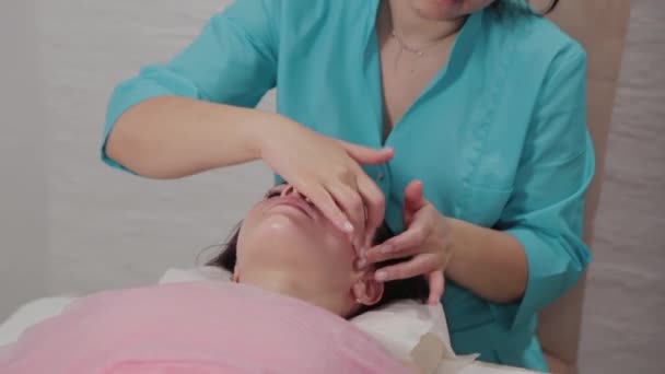 Mulher massagista terapeuta realiza massagem facial para o cliente do salão de massagem . — Vídeo de Stock