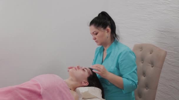 Kadın masaj terapisti masaj salonunun müşterisine yüz masajı yapar.. — Stok video
