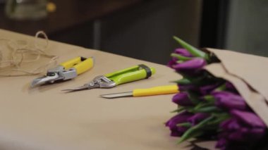 Çiçekçilerin çalışma aletleri çiçeklerle dolu bir masada yatıyor..