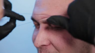 Kaşlar, güzellik salonundaki bir adama iplikle kaş düzeltme yapar..