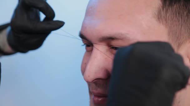 Browist fait correction des sourcils avec un fil à un homme dans un salon de beauté . — Video