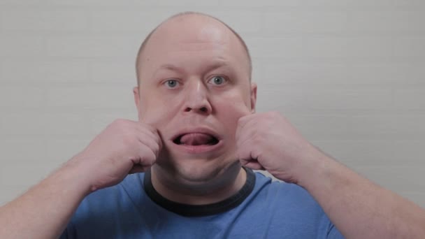 En skallig man sträcker på kinderna vid kameran. Porträtt av en skallig man. — Stockvideo