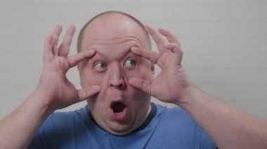 Kel adam ellerini kameraya dayayarak gözlerini sonuna kadar açar. Kel bir adamın portresi.