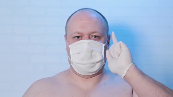 Een man met een medisch masker speelt op de camera. — Stockvideo