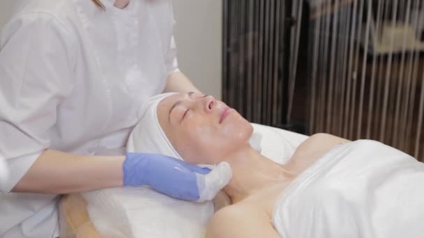 Professionell kosmetolog tvättar masken från ansiktet på en kvinna. — Stockvideo