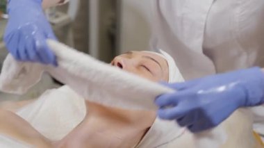Profesyonel bir güzellik uzmanı bir kadına havluyla yüz sarıyor. Kozmetoloji.
