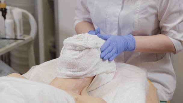 Eine professionelle Kosmetikerin wickelt einer Frau ein Gesicht mit einem Handtuch ein. Kosmetologie. — Stockvideo