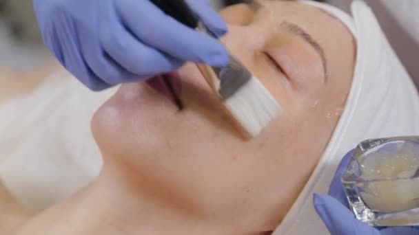 Επαγγελματίας αισθητικός που εφαρμόζει μάσκα προσώπου σε μια γυναίκα. — Αρχείο Βίντεο