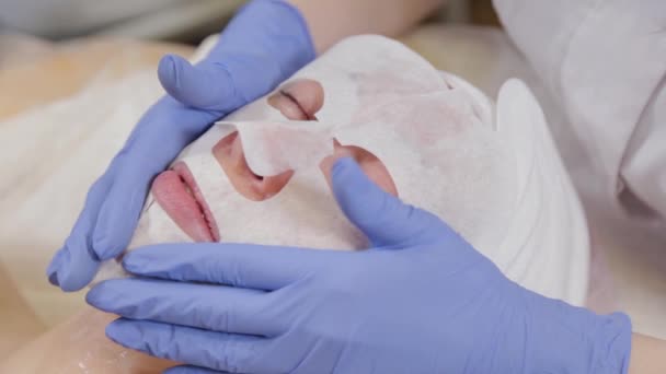 専門家は女性クライアントに顔マスクを置きます.化粧品. — ストック動画