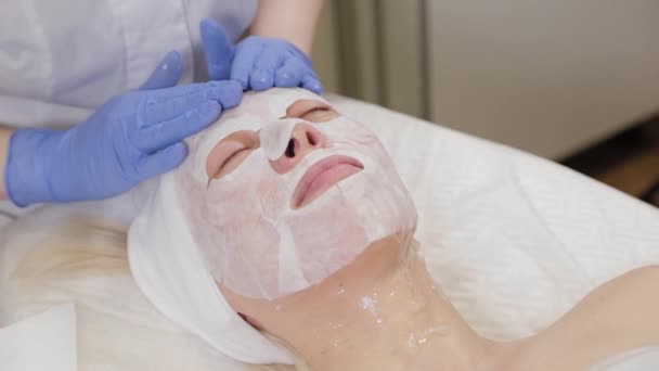 Professional puts face mask to woman client. Cosmetology. — Stock Video