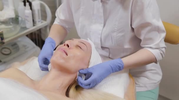 Professionell kosmetolog tvättar masken från ansiktet på en kvinna. — Stockvideo