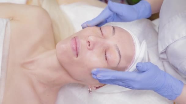 Il professionista applica la crema al viso di una cliente donna. Cosmetologia . — Video Stock