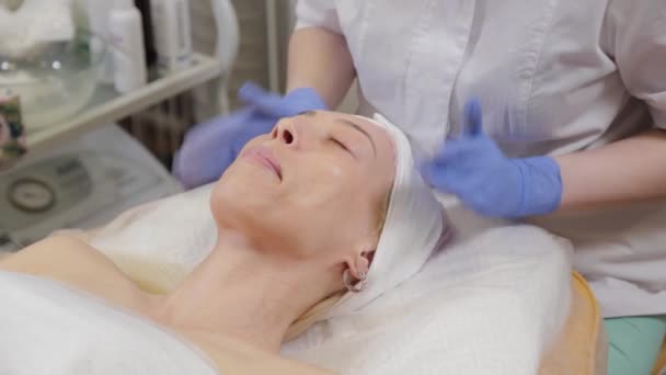 Il professionista applica la crema al viso di una cliente donna. Cosmetologia . — Video Stock