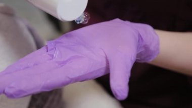 Profesyonel güzellik uzmanı eldivenlere jöle sürer ve ovalar..