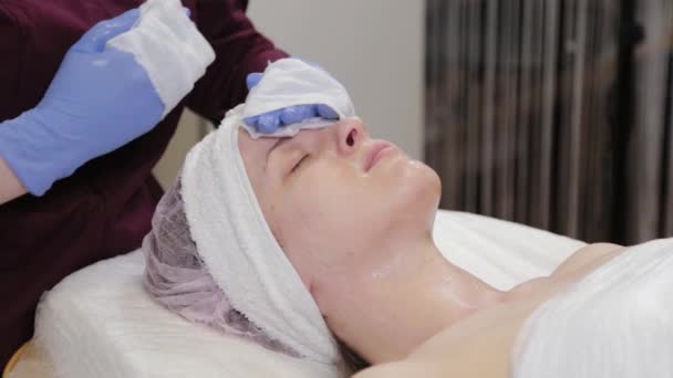 Професійний косметолог вимиває маску з обличчя жінки . — стокове відео