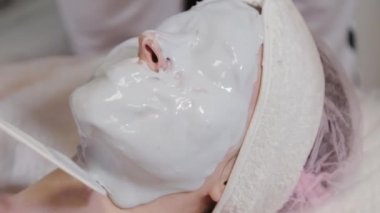 Profesyonel güzellik uzmanı bir kadına yüz maskesi takıyor..