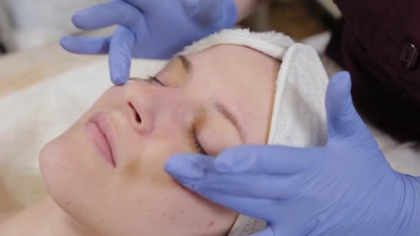 Esteticista profissional aplica hidratante a um rosto de mulher . — Vídeo de Stock