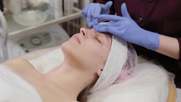 Professionell kosmetolog applicerar fuktighetskräm på en kvinnas ansikte. — Stockvideo