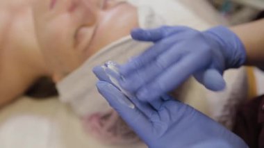 Profesyonel güzellik uzmanı bir kadının yüzüne nemlendirici sürüyor..