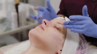 Profesyonel güzellik uzmanı bir kadının yüzüne nemlendirici sürüyor..