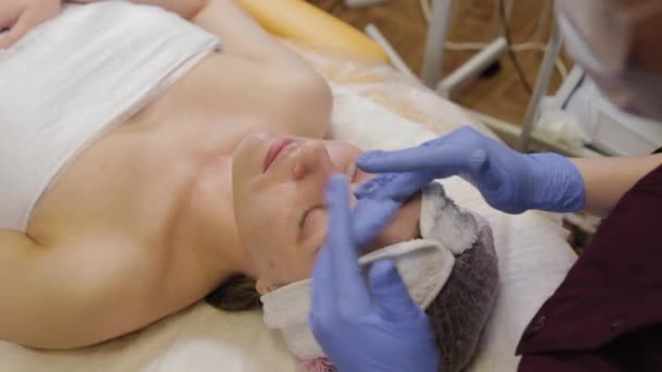 Επαγγελματική beautician εφαρμόζει ενυδατική κρέμα σε ένα πρόσωπο womans. — Αρχείο Βίντεο