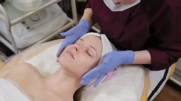 Bir kadının yüzüne masaj yapan profesyonel bir güzellik uzmanı.. — Stok video