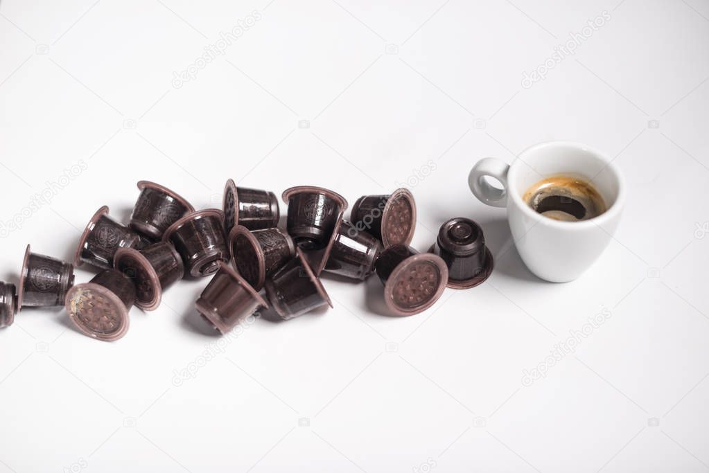 Used coffe capsules and espresso coffee over a white background.
