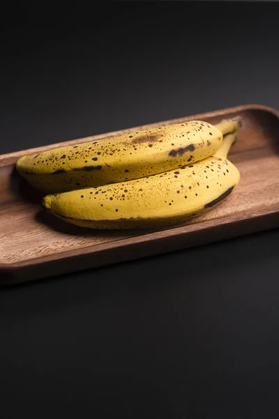 Two organic bananas in a wood sish over a black board. — Stock Photo, Image