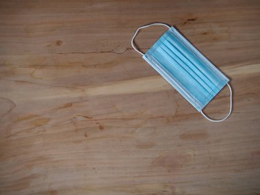 Ağzını ve burnunu lastik kulaklıklarla kapatmak için 3 katlı mavi cerrahi maske. Bakteri ve morfinden koruma maskesi. Tahta zemine uzan. Koruma kavramı.