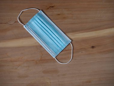 Ağzını ve burnunu lastik kulaklıklarla kapatmak için 3 katlı mavi cerrahi maske. Bakteri ve morfinden koruma maskesi. Tahta zemine uzan. Koruma kavramı.