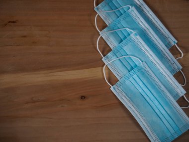 Ağzını ve burnunu lastik kulaklıklarla kapatmak için 3 katlı mavi cerrahi maske. Bakteri ve morfinden koruma maskesi. Tahta zemine uzan. Koruma kavramı.