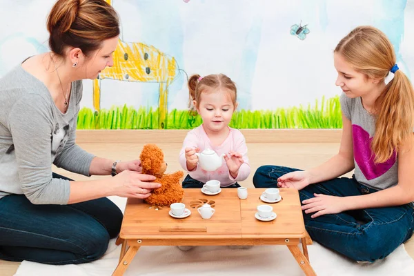 Malá dívka si hraje s maminkou a sestrou na tea party pomocí dítě — Stock fotografie