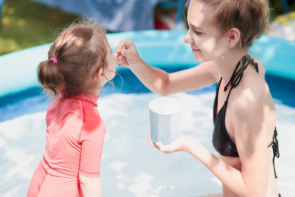 Genç kız küçük kız kardeşi bir bahçe içinde yüzme havuzunda birlikte vakit ile bir yaz güneşli gün dondurma yeme keyfini çıkarın. Aile vakit — Stok fotoğraf