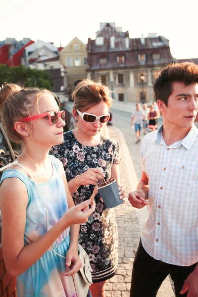 Family spending time together in the city centre enjoy eating ice cream on a summer day. Mother, teenage girl and boy spending quality time on sunny afternoon eating sweet dessert. Downtown area, old town in the background — Stock Photo, Image