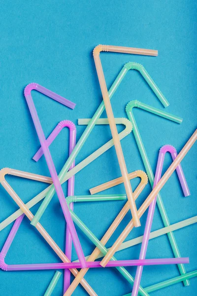 Mavi arkaplana saçılmış bir yığın plastik içecek pipetleri.