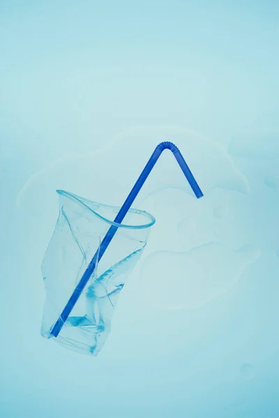 Squashed plastic cup and drink straw over blue background — Stock Photo, Image
