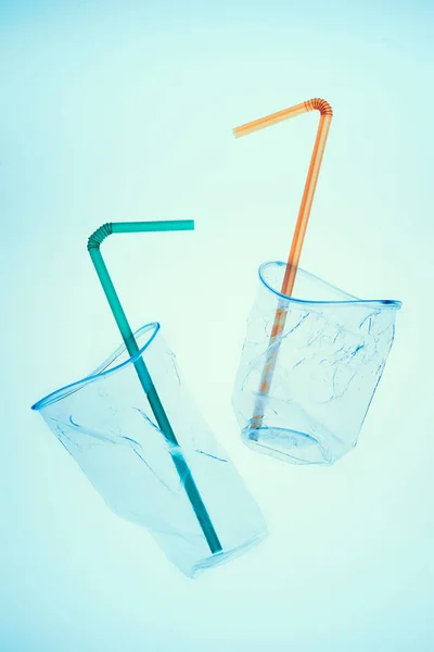 Squashed plastic cups and drink straws over blue background