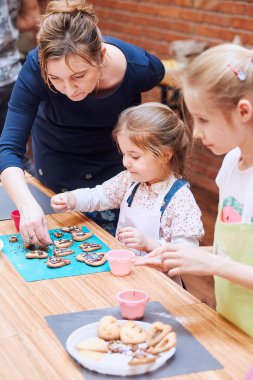 Küçük kız annesinin yardımıyla renkli şekerle ve şekerle pişirilmiş kurabiyeleri süsledi. Çocuk fırın atölyesinde çalışıyor. Çocuklar için yemek pişirme dersleri, hevesli küçük şefler. Yemek yapmayı öğreniyorum. Hazırlanmış malzemelerin birleştirilmesi ve karıştırılması
