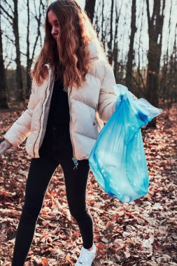 Ormanı temizleyen genç bir kadın. Poşetlere plastik atık toplayan bir gönüllü. Plastik kirliliği ve çok fazla plastik atığı kavramı. Çevresel bir sorun. Çevresel hasar. Çevreye karşı sorumluluk. Gerçek insanlar, otantik durumlar.