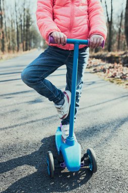 Parkta oynayan, scooter süren, güneşli bir sonbahar gününde eğlenen küçük bir kız. Gerçek insanlar, otantik durumlar.