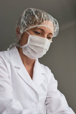 Yüzü maskeyle kaplı bir doktor. Virüs bulaşmasını önlemek ve hastalığın yayılmasını önlemek için üniforma, şapka ve maske takan genç bir kadının portresi. Gerçek insanlar, otantik durumlar.
