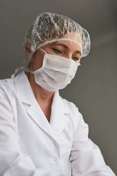Doctor with face covered with mask. Portrait of young woman wearing the uniform, cap and mask to avoid virus infection and to prevent the spread of disease. Real people, authentic situations
