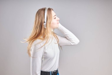 Müzik dinleyen genç bir kız video izlerken eğleniyor arkadaşlarıyla sohbet ediyor akıllı telefon kulaklıkları takıp gri arka planda dikiliyor.