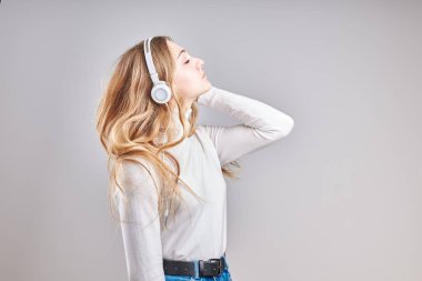 Müzik dinleyen genç bir kız video izlerken eğleniyor arkadaşlarıyla sohbet ediyor akıllı telefon kulaklıkları takıp gri arka planda dikiliyor.