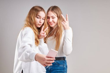 Birlikte müzik dinleyen genç kızlar video izleyerek eğleniyorlar görüntülü sohbet yapıyorlar arkadaşlarla sohbet ediyorlar akıllı telefon kulaklıkları takıp gri arka planda duruyorlar.