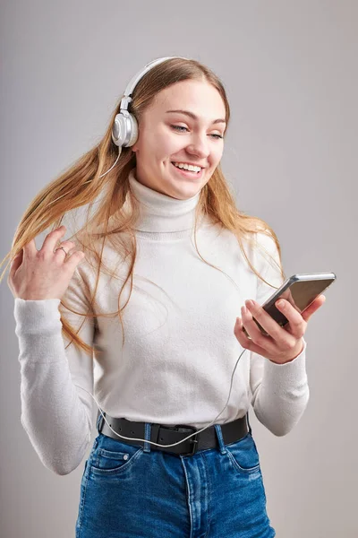 年轻女子在观看音乐流媒体内容时 喜欢看视频 喜欢和朋友们用智能手机耳机在灰蒙蒙的背景下做手势聊天 — 图库照片