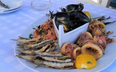  Büyük beyaz bir tabakta sağlıklı deniz ürünleri, kızarmış balık, karides, midye, kalamar eti, Yunan mutfağı.