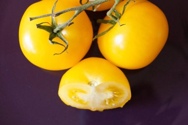 Koyu arkaplanda sarı domatesler. İki tane tam meyve ve bir tane de yarı meyve makro fotoğrafıyla kesilmiş.