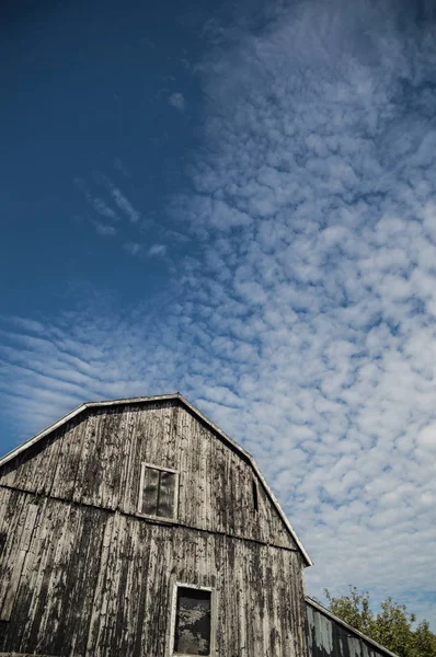 伝統的な古いオンタリオ入母屋屋根納屋 黒だった 風化とボードの抽象的な広角は太陽の光でライトアップ 空ある絹雲の興味深い満田衛資とディープ ブルーの背景として — ストック写真